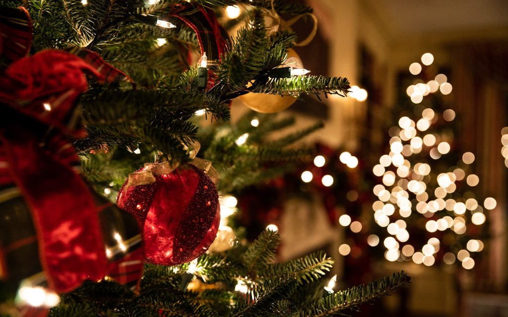 God jul og godt nytt år fra Takstmann Spira Takst: Nærbilde av et pyntet juletre med glitrende kuler og lys i varm atmosfære.